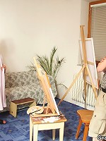 The redhead opens her robe and poses for the two guys painting her naked body